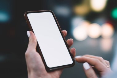 Tanımlanamayan bir kadın, şehrin boş zamanlarında cep telefonunda internet uygulamasında sörf yaparken bulanık arka planda aydınlanmış ışıkların yanında duruyor.