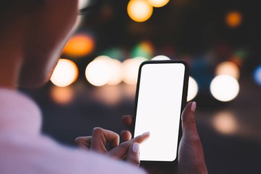 Şehrin arka planında Bokeh ışıkları ile sokakta dikilirken meçhul kadın cep telefonuna ve boş beyaz ekrana dokunuyor.