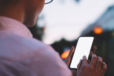 Alacakaranlıkta şehir caddesinde duran tanınmayan çağdaş kadın ve mesaj iletileri için boş ekran ile cep telefonuna göz atmak