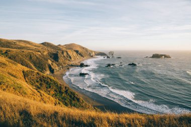 Güneşli bir günde, kayalık kıyılarda mavi gökyüzüne vuran beyaz köpüklü deniz dalgalarından.