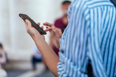 Arka planda, arkadaşlarıyla cep telefonunda sohbet eden ve şehir merkezinde dinlenirken Vatikan 'da fotoğraf ve zaman geçiren bir kadın görülüyor.