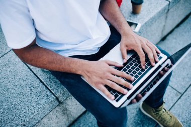 Şehrin taştan bankında dizüstü bilgisayar üzerinde çalışırken gündelik giysiler içinde tanınmayan siyahi bir erkek serbest yazar.