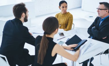 Ekonomik ticareti analiz eden deneyimli yöneticilerden oluşan bir grup, çeşitli meslektaşlar, üretken beyin fırtınası sırasında taslak çizimleri ve pazarlama planını tartışıyor.