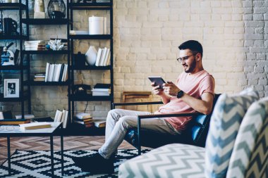 İnternet sitesine bağlanmak ve dokunmatik ped teknolojisi ile online oyunlar oynamak için WIFI 'ye bağlanan görsel koruma için optik gözlüklü bir erkek, bin yıllık hipster adam sohbet ediyor ve mesajlaşıyor