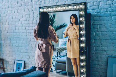 Kafkas kadın modacı, lamba aynasının yanında poz veriyor. Soyunma odasında arka plan ışığı var. Bugün için şık kıyafetler seçiyor.