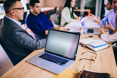 Finansal internet reklamları için kopyalama alanı olan dizüstü bilgisayara seçici odaklanma, ofiste çalışırken boş teknolojiyi tartışan erkek ve kadın meslektaşlar grubu