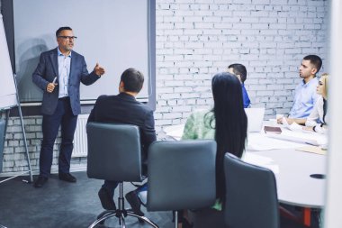 Resmi olarak giyinmiş ofis çalışanları iş projesinde işbirliği yapıyor şirket yönetim kurulu odasında konuşuyor, olgun yönetici firmada beyin fırtınası sırasında deneyim paylaşımı yapıyor