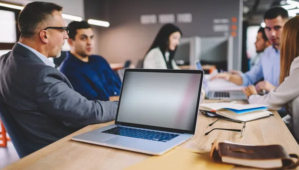 Finansal internet reklamları için kopyalama alanı olan dizüstü bilgisayara seçici odaklanma, ofiste çalışırken boş teknolojiyi tartışan erkek ve kadın meslektaşlar grubu