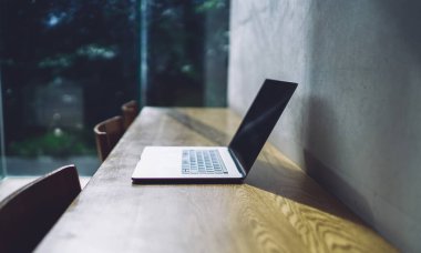 Masanın üzerindeki dizüstü bilgisayarın kapağı kapalı. Duvarın yanına, pencere manzarasının bulanık arka planına yerleştirilmiş sandalyeler var.