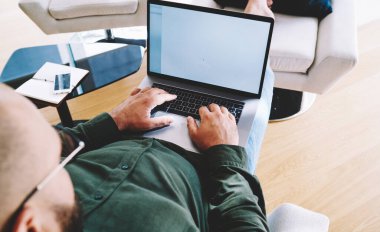 Modern oturma odasında modern dizüstü bilgisayar üzerinde çalışırken rahat bir pozisyonda oturan serbest çalışan bir yönetici.