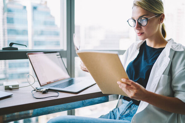 Crop female manager sitting at table with laptop and reading report while working on new business project in modern office