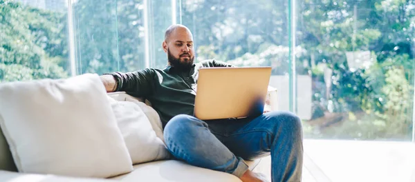 穿着休闲装的广角型男人坐在柔软的沙发上 膝上型笔记本电脑 一边工作一边寻找信息 — 图库照片