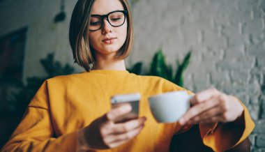 Gözlüklü genç web blogcusu, halka açık kablosuz internet bağlantısını kullanarak yerel kahve dükkanını ziyaret ederken kısa mesajlar yazıyor, Kafkasyalı milenyum kadını akıllı telefondan medya içeriğini tarıyor