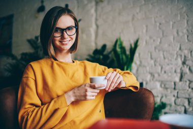 Kafenin iç kısımlarında hafta sonu kameraya gülümseyen Kafkasyalı mutlu bir müşterinin portresi, kafeteryada poz vermek için optik gözlüklü güzel bir kız.