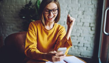 Klasik gözlüklü neşeli kadın cep telefonu teknolojisindeki kafe internet bağlantısını kullanarak gelen e-posta mesajından memnun, akıllı telefon aygıtında çevrimiçi yorumları okuyan güler yüzlü blog yazarı