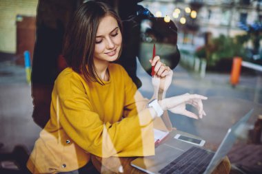 Modern dizüstü bilgisayarı olan, beyaz kadın serbest çalışan, giyebilen akıllı saati kontrol eden, sergi aletlerine bakan yetenekli hippi kız.