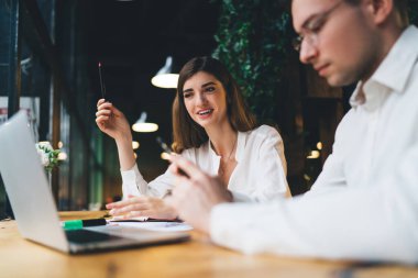 Beyaz bluzlu, elinde kalemle gülümseyen genç bir kadın. Günlük kıyafetleriyle dikkatle dizüstü bilgisayara bakıyor.