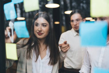 İş görüşmelerinde pazarlama planlarını tartışırken pencerenin yanında durup notlar alan bir grup pozitif insan