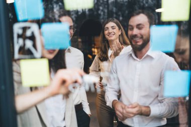 Moda kıyafetleri içinde neşeli işçiler pencerenin yanında durup toplantı sırasında iş planı hakkında sohbet ediyorlar.