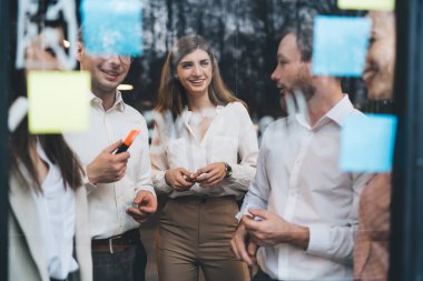 Takım çalışması sırasında yan yana duran ve şirket ofisinde çalışırken gelecekteki projenin sonuçlarını tartışan iyimser iş arkadaşları