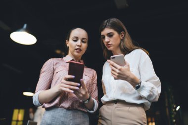 Resmi kıyafetler ve kol saati takan, cep telefonuyla internette sörf yapan, haberleri paylaşan, çağdaş ofiste çalışan ve proje üzerinde çalışan kadın çalışanların düşük açısı.