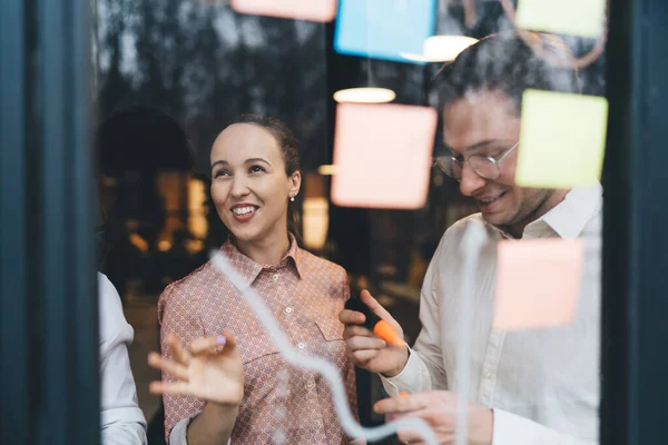 Yeni iş projesinde birlikte çalışırken modern çalışma alanının penceresinin yanında duran serbest giyinen pozitif bir çift.