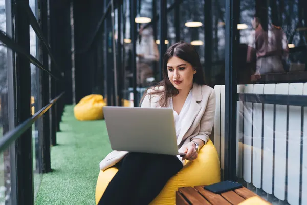 Konzentrierte Frau Lässiger Kleidung Sitzt Auf Einer Sitzsäcke Und Arbeitet — Stockfoto