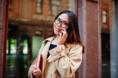 Dişli tebessümlü Asyalı kadının elinde not defteriyle caddede durup cep telefonuyla kameraya bakmasına sevindim.