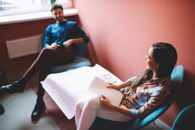 Yüksek açılı gülümseyen genç bayan mimar. Gazete ve kalemle iş arkadaşıyla yeni inşaat planlarını tartışıyor.