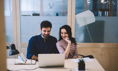 İş yerindeki bilgisayar ekranına bakarken projeyi düşünen ve neşeli bayan meslektaşla tartışan sakallı olumlu bir erkek yönetici.