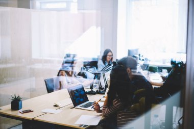 Gündüz vakti modern ışık ofisinde dizüstü bilgisayarla iş projesinde birlikte çalışan konsantre iş arkadaşlarının cam arkası bakış açısıyla.