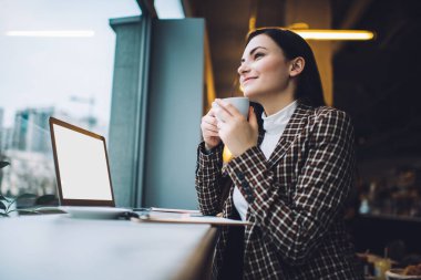 Düşük açılı, mutlu, zeki, serbest çalışan, sıcak bir şeyler içen ve kafeteryada dizüstü bilgisayarla yan yana oturan biri.