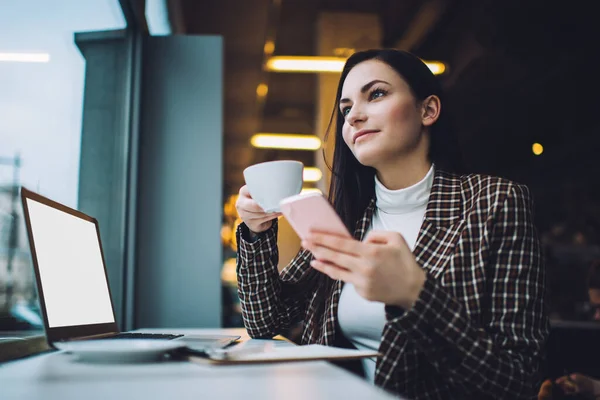 若い女性マネージャーの低い角度携帯電話を閲覧しながらコーヒーブレイクオフィスでノートパソコンと机に座っている — ストック写真