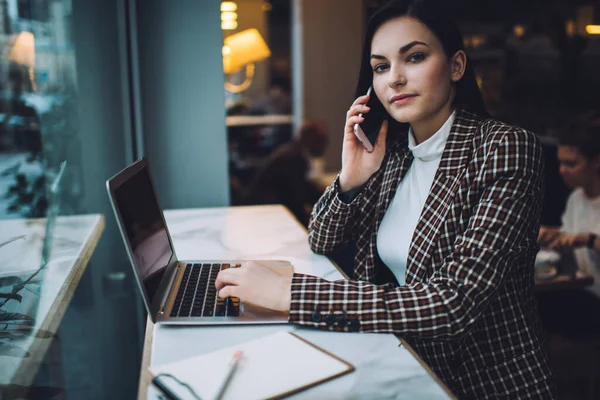 Moda kıyafetli, yeni projeyi tartışan ve kafede çalışırken kameraya bakan genç ve ciddi bir kadın serbest yazar.