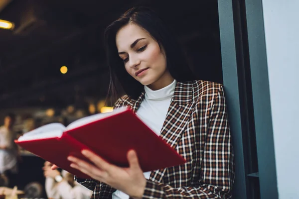 Kafe duvarına yaslanmış zarif kıyafetli genç bir bayanın elinde açık bir not defteriyle durduğu yerden.