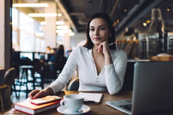 Hüsnükuruntulu uzaktan kumandalı kadın. Kafede masa başında elinde kalem ve panoyla kameraya bakıp proje fikrini düşünüyor.
