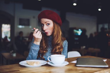 Modern kafede tatlı ve kahvenin tadını çıkarırken bereli ve günlük kıyafetli pozitif bir bayan gözlerini kaçırıyor.