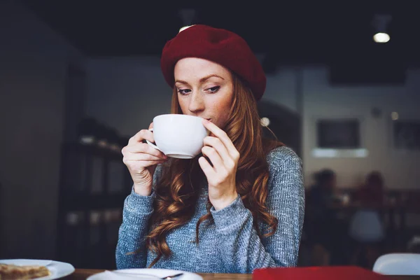 夢のような女性でベレー帽で長い髪持ち上げるカップの熱い飲み物に唇と離れて見ながらコーヒーショップで一人で休憩 — ストック写真