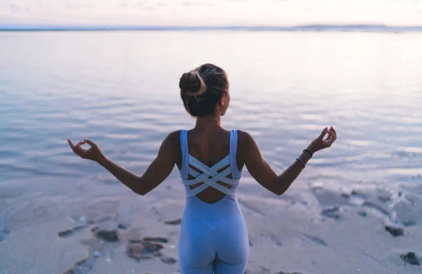 バックビューのスリム女性ヨギ取得エネルギーインスピレーションと禅から自然環境を過ごすレジャーで海岸 穏やかな女の子でトラックスーツ海の近くに朝の瞑想中に手を上げる — ストック写真