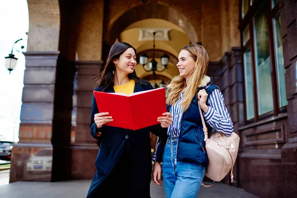 穿着休闲装的现代快乐女学生站在历史名牌大学附近 一边看书一边相互凝视着对方 — 图库照片