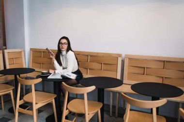 Hafif kafede dikkatlice bakışlarını kaçırarak telefonda günlük kıyafetlerini giyip mesajlaşan odaklanmış bir kadından.