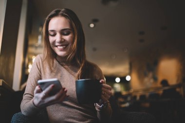 Sıradan kıyafetlerle gezen, cep telefonuyla sohbet eden, mesajları okuyan, fincandan çay içen ve rahat bir barda dinlenen iyimser bir kadın.