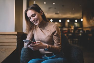 Kol saatli olumlu genç bayan cep telefonundan mesaj atıyor ve haftasonu yaratıcı kafeteryada dinlenirken gülümsüyor.