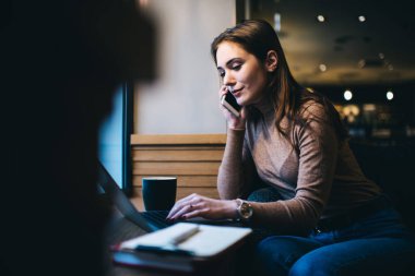 Gündelik giysiler içinde serbest çalışan, dizüstü bilgisayarlı ve klavyeli bir kadın. Proje üzerinde çalışırken ve telefonla konuşurken.