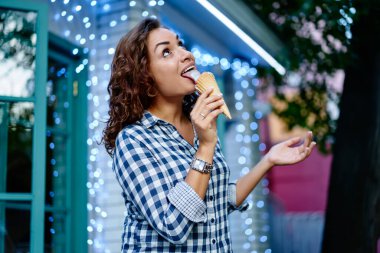 Gündelik gömlekli çekici beyaz kadın konili waffle 'da tatlı tatlı meyveli tatlı yiyor yaz haftasonunun tadını çıkarıyor genç hippi kız seyahat tatillerinde dondurma yiyor.