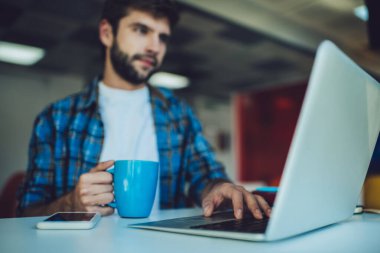 Yetenekli erkek bilişim uzmanı, çalışma alanında mesafesini korurken program kodu yaratıyor, kahve fincanı ile bulanık öğrenci dijital ağ üzerinde yazılım geliştiriyor, 4 g kablosuz ağ kullanıyor.