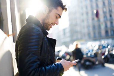 Güneşli bir günde sokakta dikilirken elinde kahve fincanı ve cep telefonu kullanan sıradan giyinen pozitiflerin yan görüntüsü.