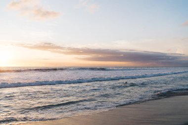 Okyanusun kumlu kıyı şeridinden inanılmaz bir manzara. Güneş batarken dalgalar ve akşam vakti sıcak, egzotik bir ülkede bulutlu bir gökyüzü.