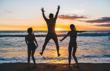 Tanınamayacak haldeki çıplak ayaklı ailenin yaz tatillerinin tadını çıkarışının ve Bali 'de akşam vakti dalgalanan deniz kıyısındaki kumlu sahilde eğlenişinin arka görüntüsü.