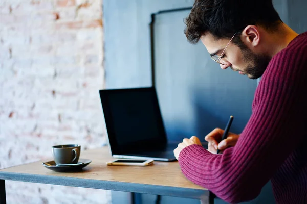 Pensivo Jovem Empresário Barbudo Óculos Tomando Notas Enquanto Trabalhava Laptop — Fotografia de Stock